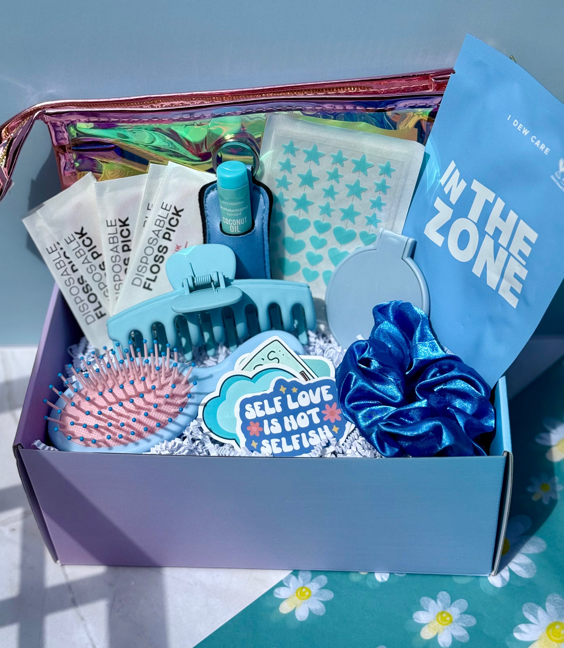 Gift box of self-care items including a scrunchie, hairbrush, and floss stick with a blue and pink color scheme.